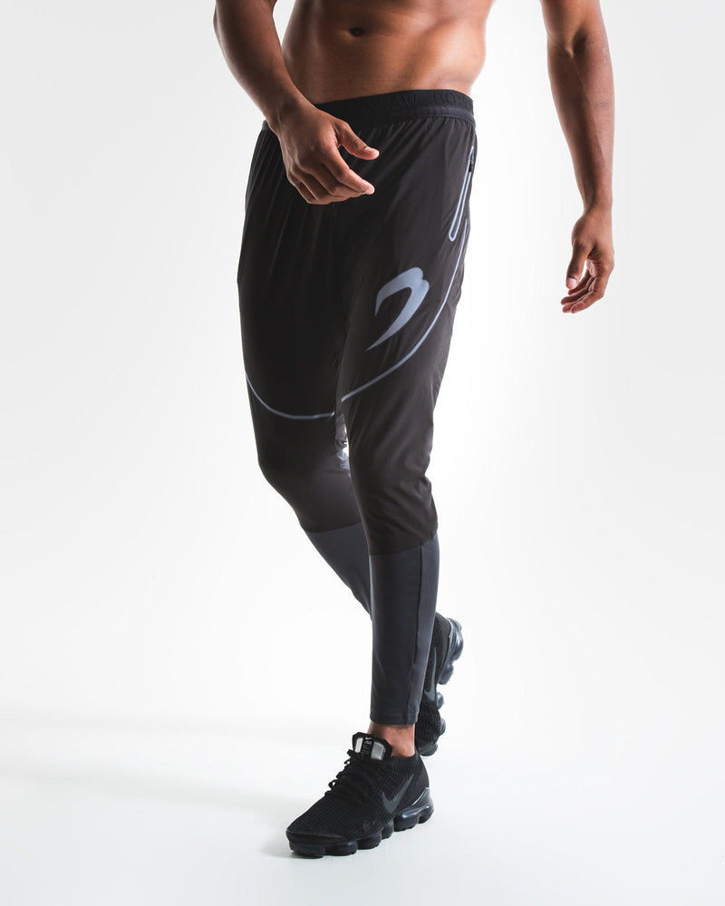 Man in slim fitting black lightweight tracksuit bottoms with reflective detailing and side zipped pockets