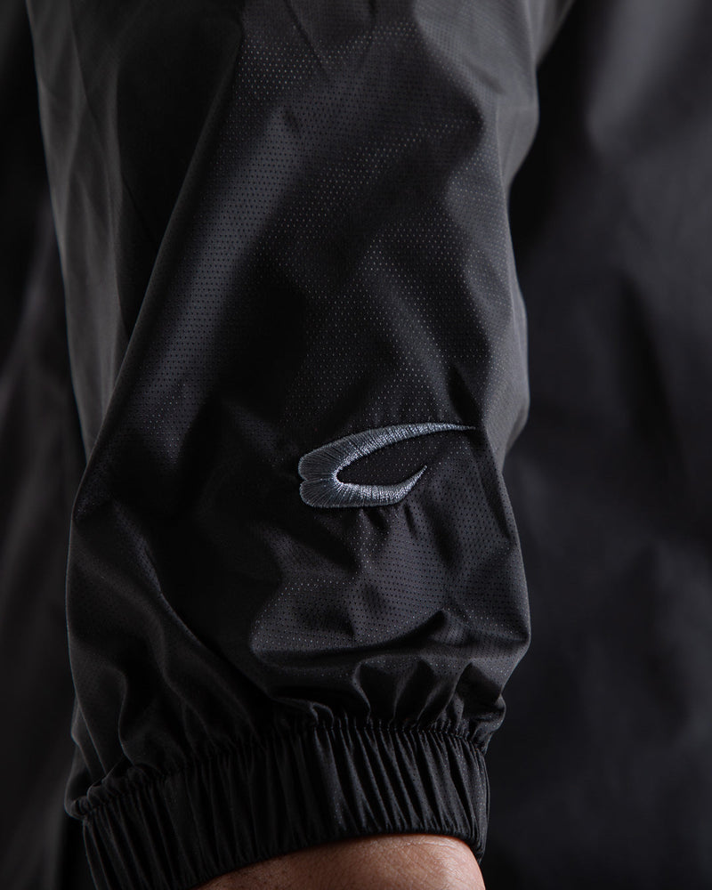 Man in black zipped windbreaker with hood and reflective big boxraw strike logo across left body panel made from nylon.