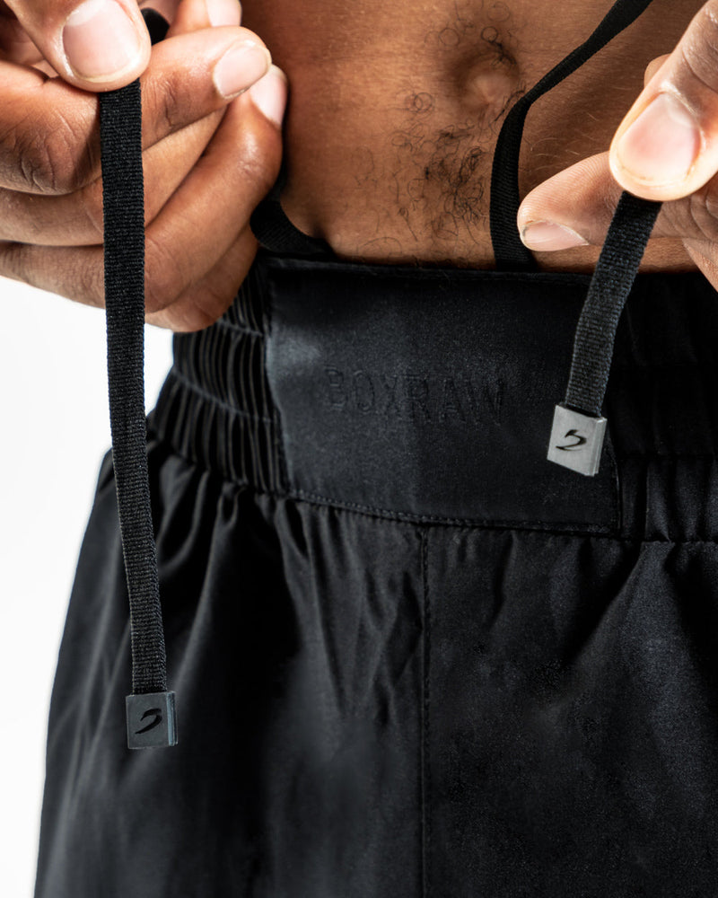 Man in black training shorts with adjustable waistband and side zipped pockets as well as an embroidered white boxraw strike logo.